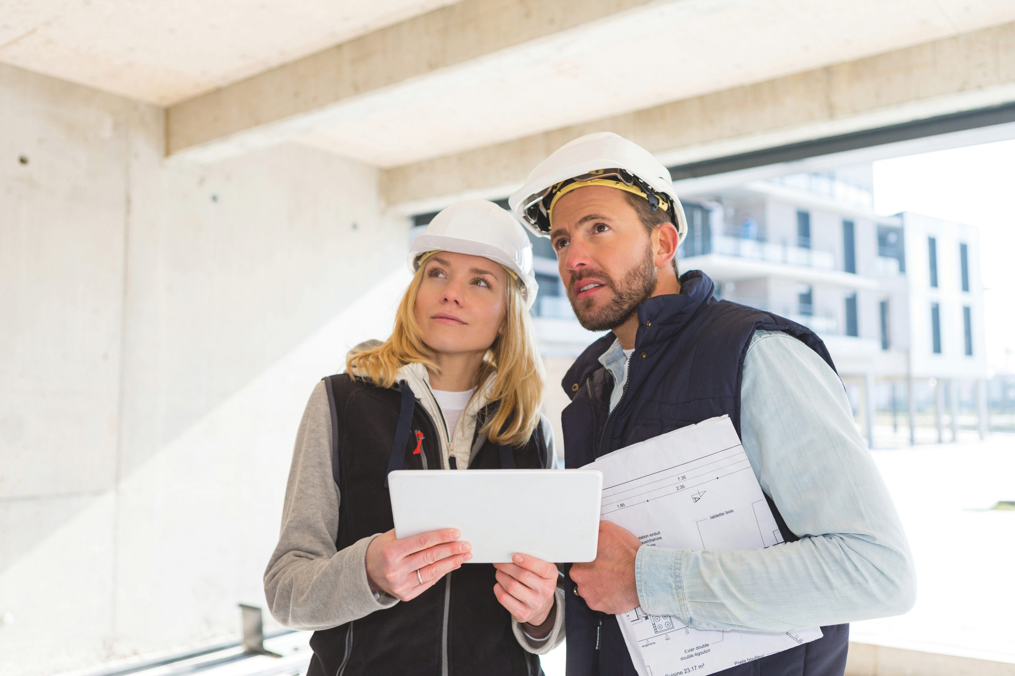 Gebäudeschaden und Reparaturmanagement: Ein Bauleiter steht mit einer Bauleiterin auf einer Baustelle und betrachten die Pläne.